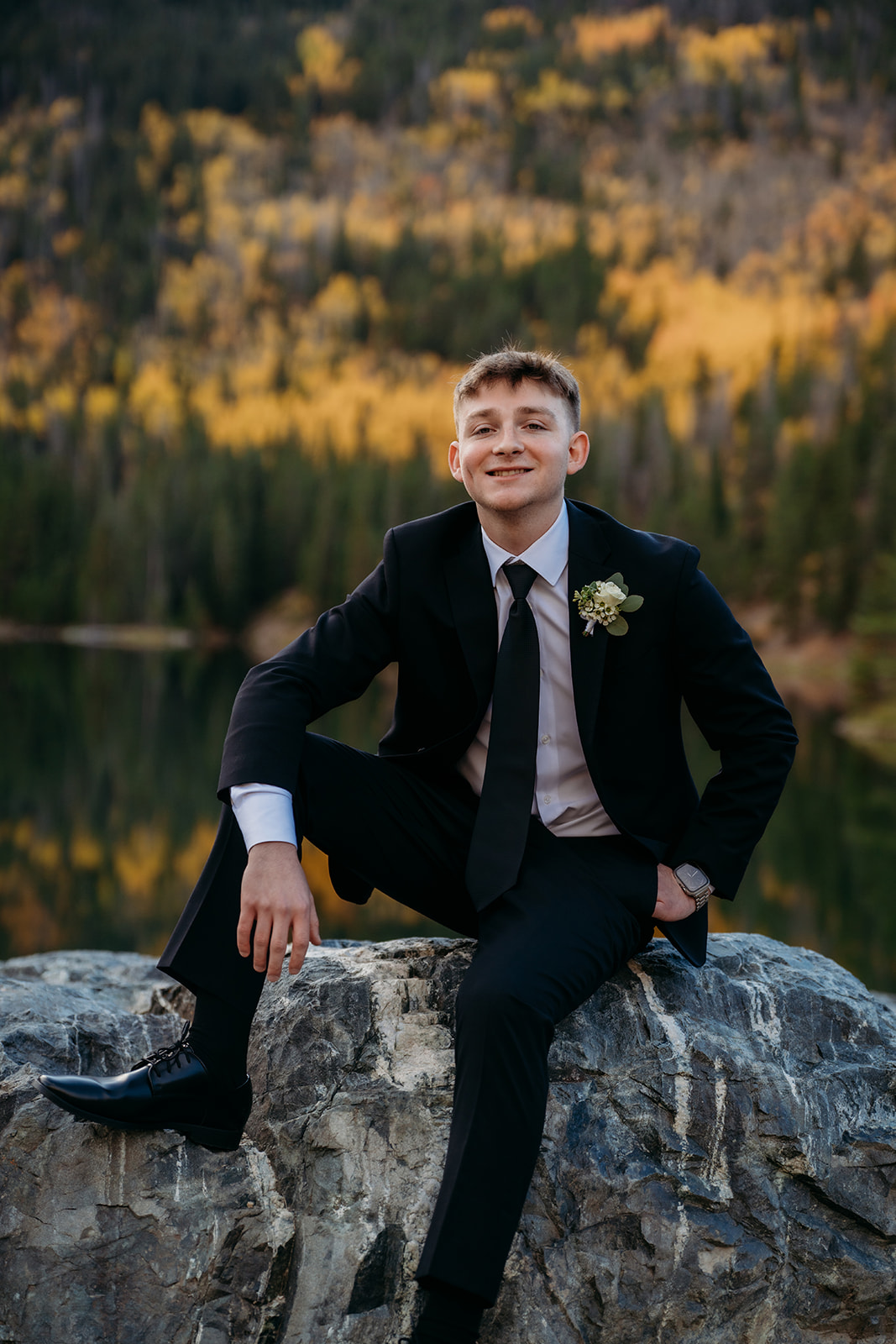 Groom sitting on boulder smiling after elopement in Colorado