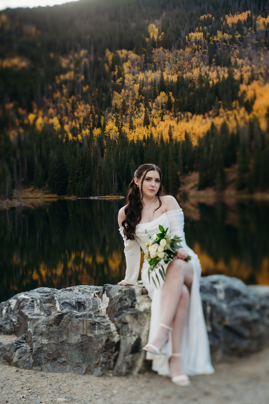 Bride sitting on rock in wedding dress while holding white floral bouquet