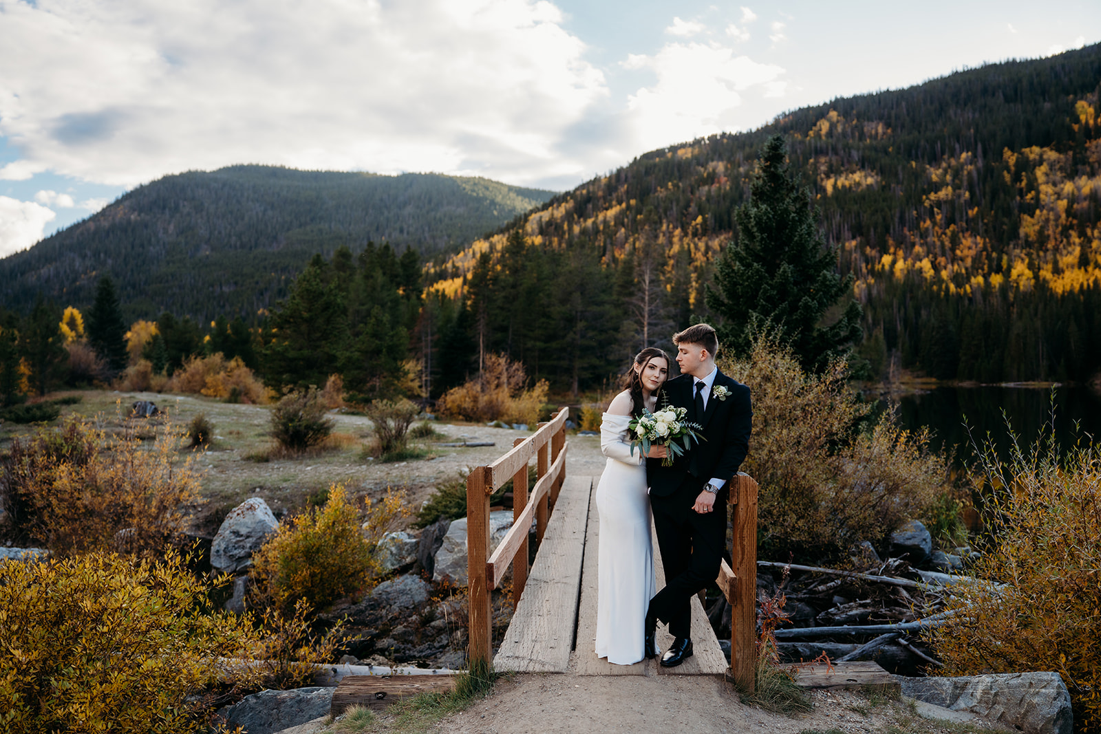 Couple leaning against bridge while groom looks over at bride leaning against him