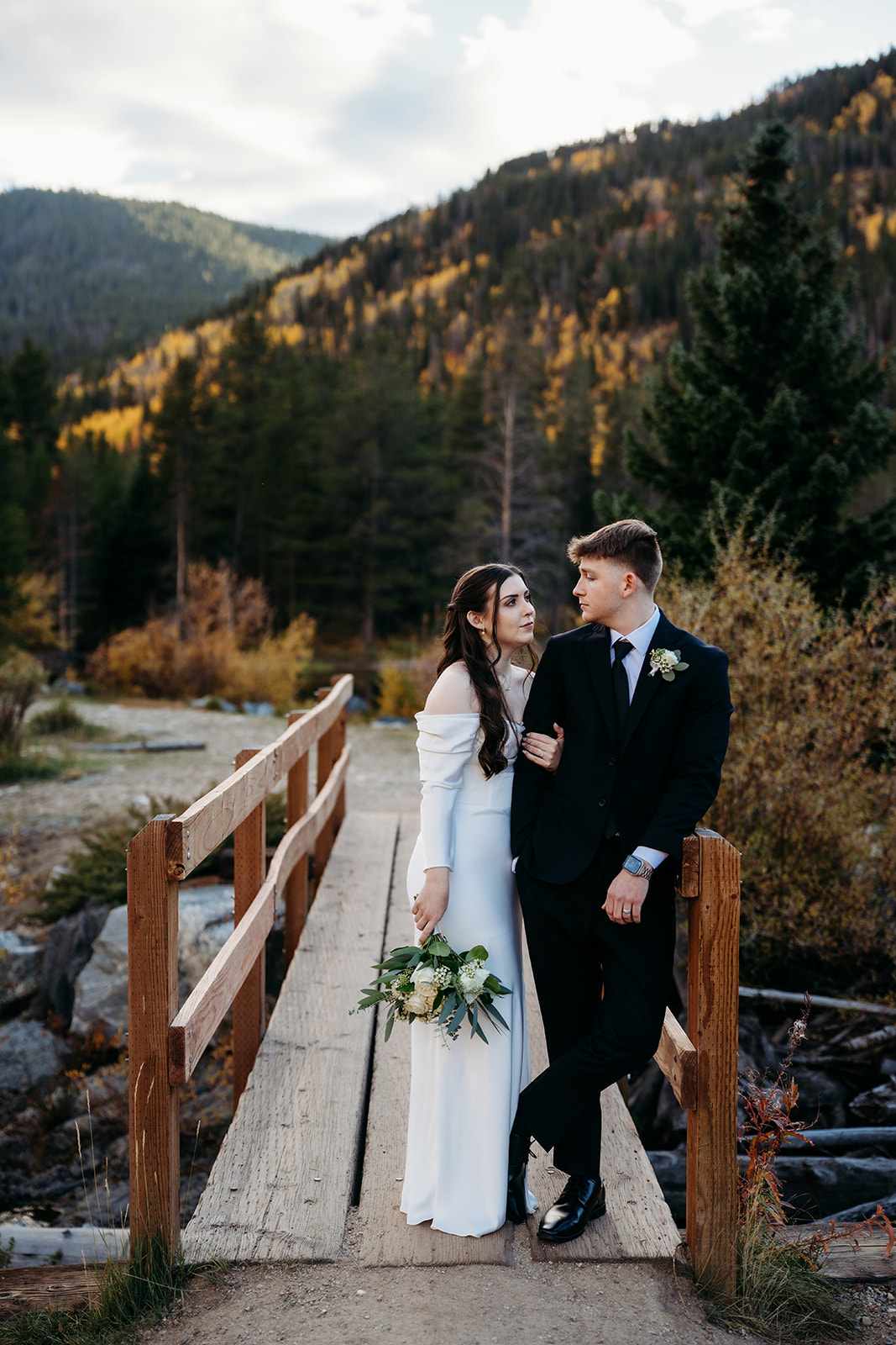 On a rustic bridge tucked in the woods, the couple leans into each other with soft smiles.