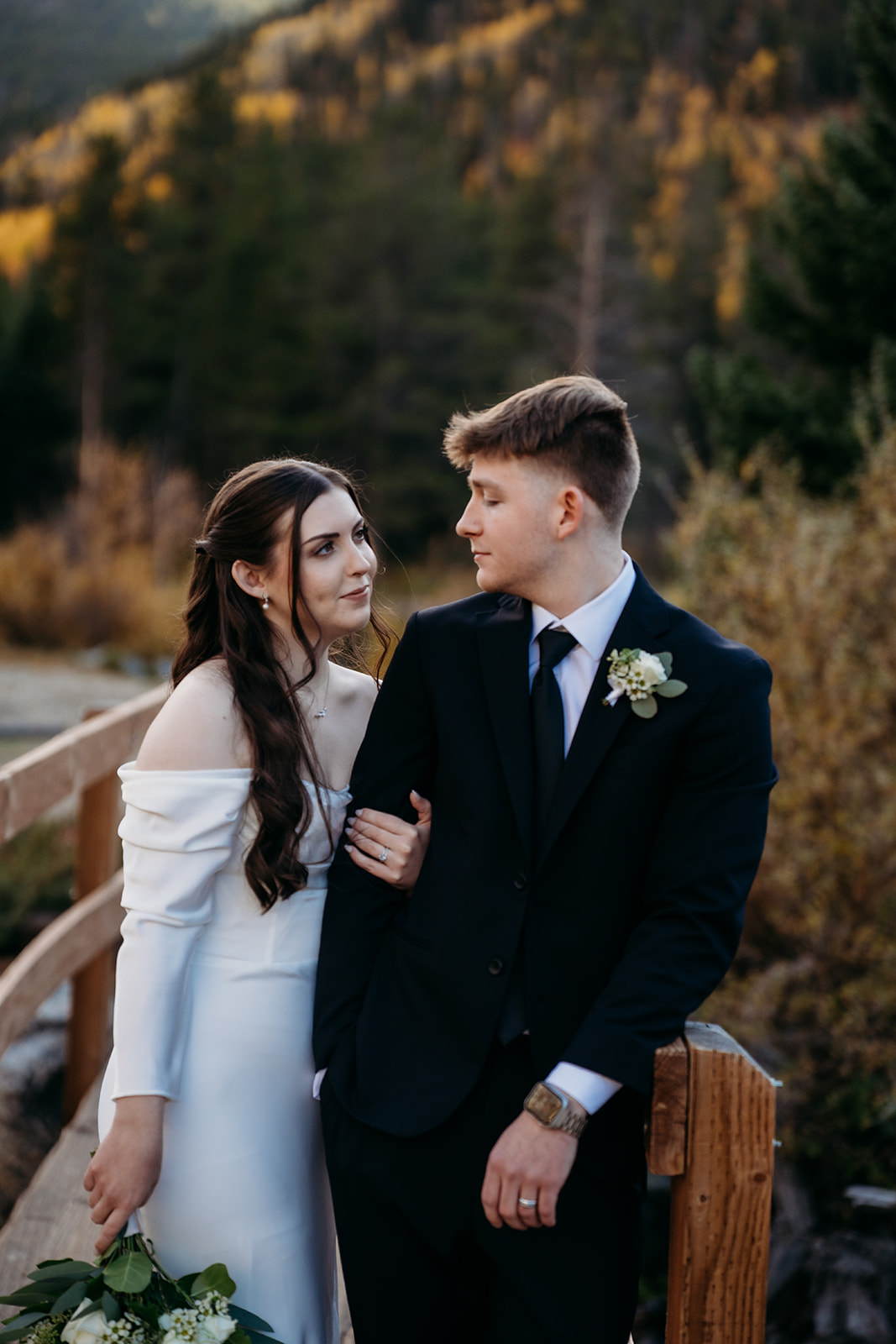 Standing on a wooden bridge surrounded by evergreens, this couple shares a quiet moment just after their ceremony.