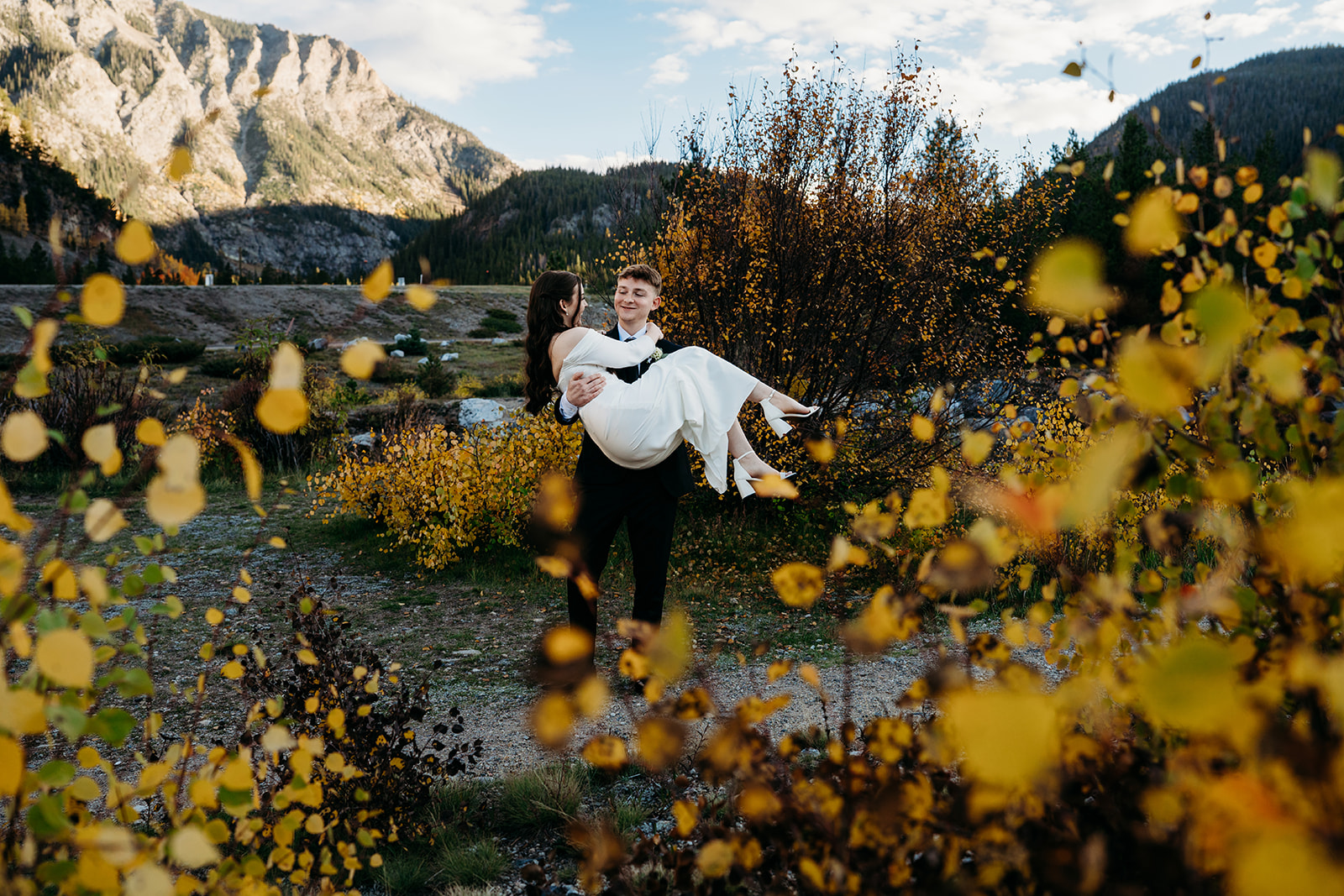 Framed by golden aspens, the groom carries his bride through a quiet mountain meadow, a joyful reminder of why couples elope to Colorado.