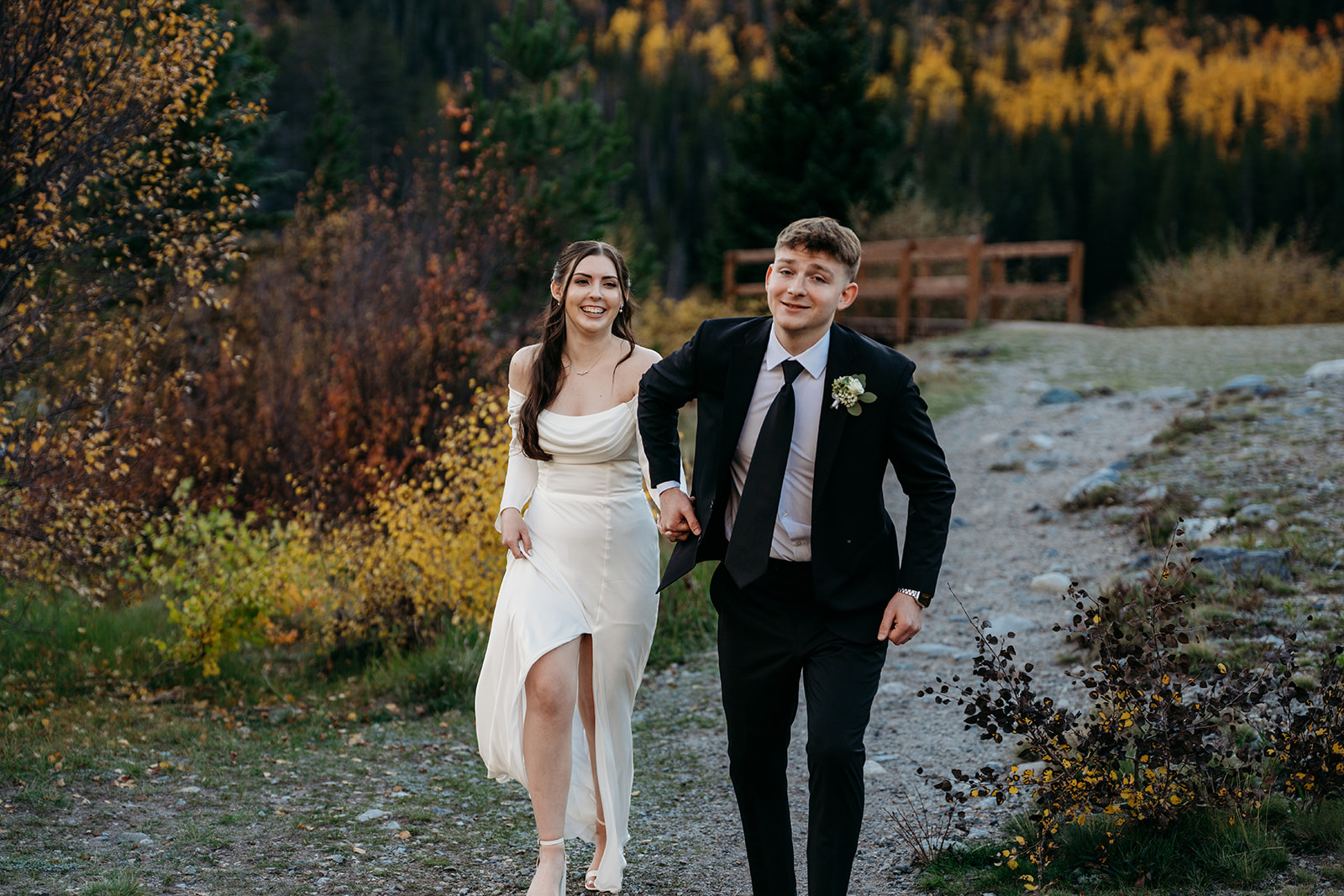 Bride and groom walking hand in hand throughout beautiful fall scenery in Colorado