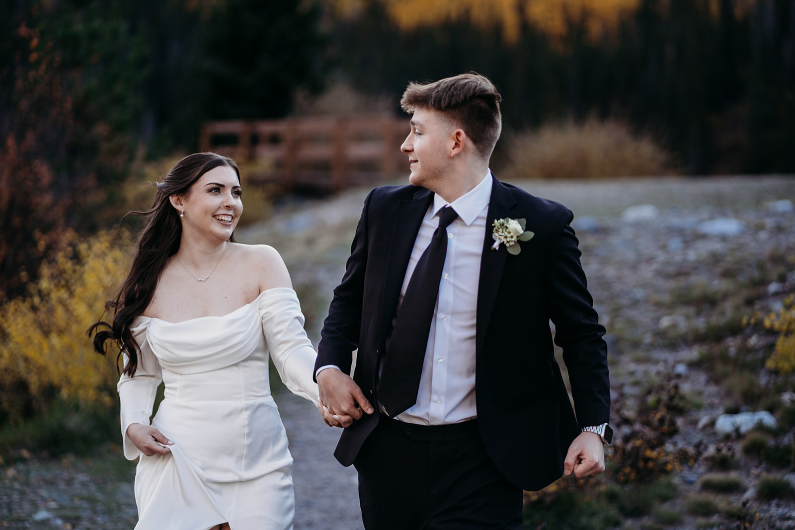 Groom holds bride's hand while looking back at her as they run away together after they elope to Colorado