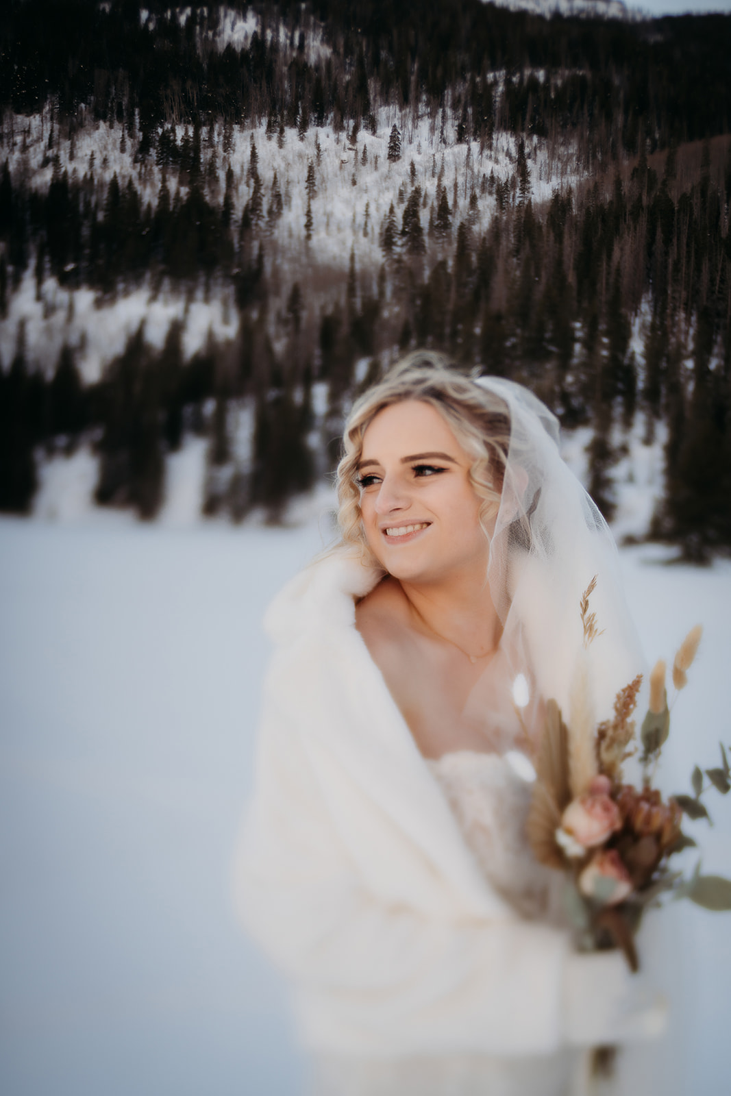 Bride smiling while holding a bouquet, dressed in a fur wrap—an elegant example of winter wedding outfits for colder temps.