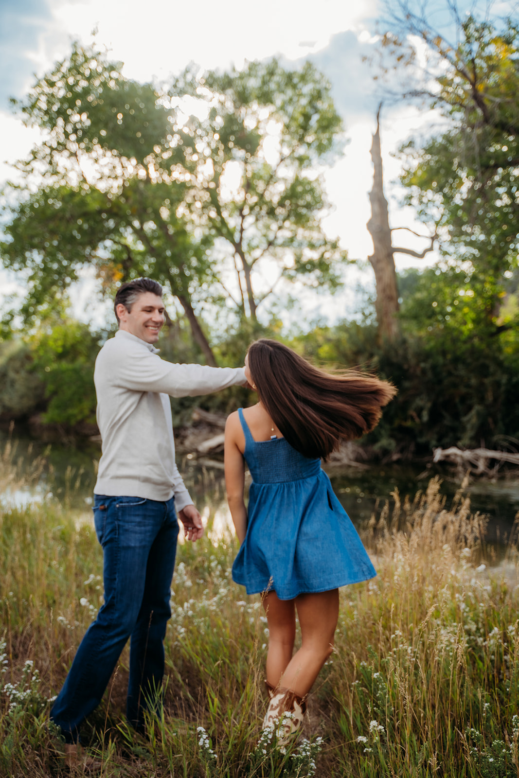 A dad twirls his daughter playfully in the field, both laughing as the sunlight filters through the trees.