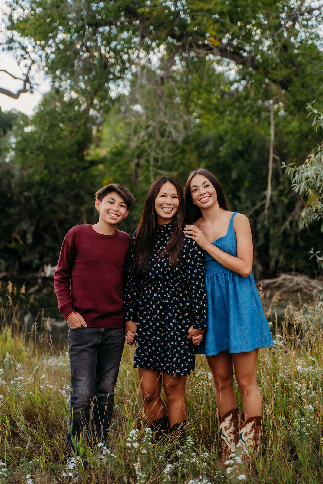 The trio of mom and kids pose closely in the grass, all dressed in rich fall tones and natural smiles.