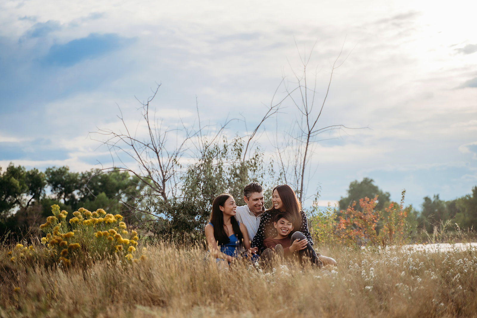 Cuddled up in tall grass by the water, this family shares a quiet moment full of connection and smiles.