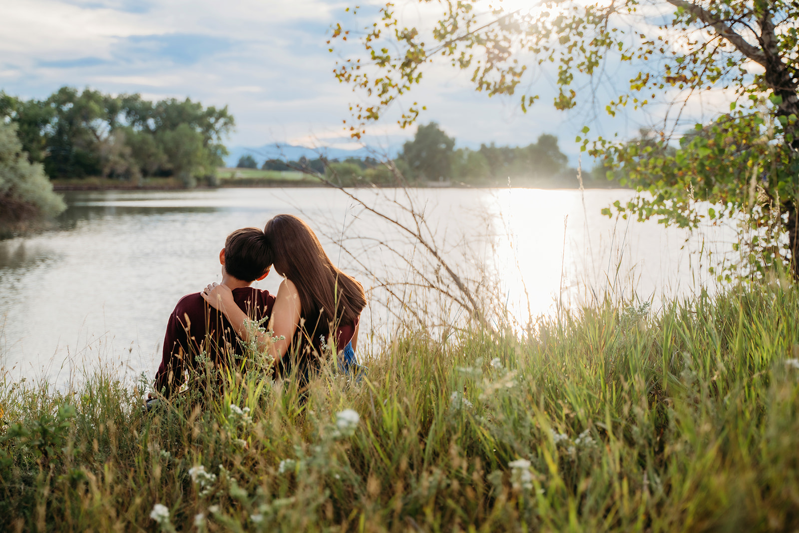 A quiet lakeside moment shared between siblings, gazing at the water as the sun sets behind them.