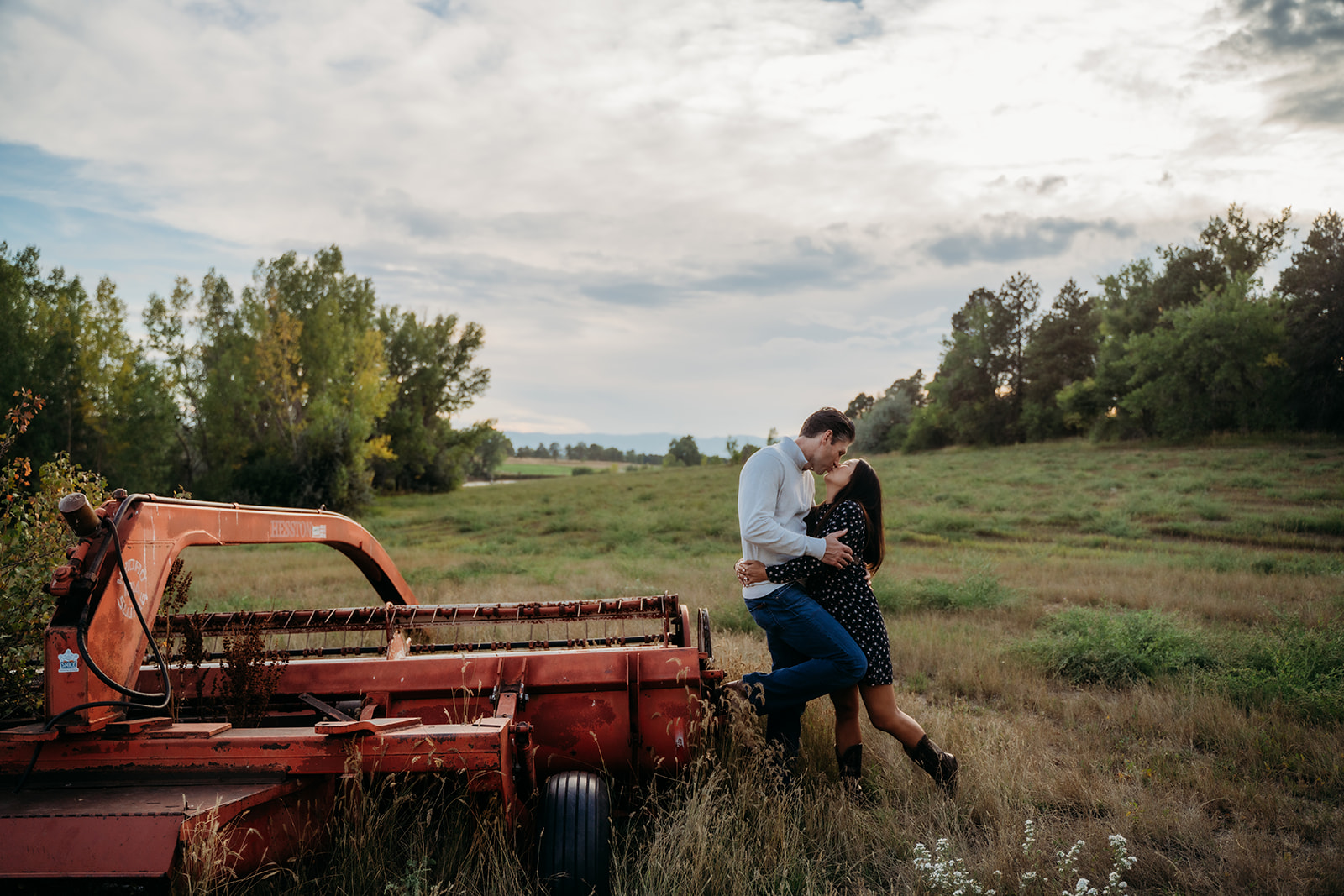Parents steal a romantic kiss beside an old red tractor, adding a sweet personal touch to their family outdoor pictures.