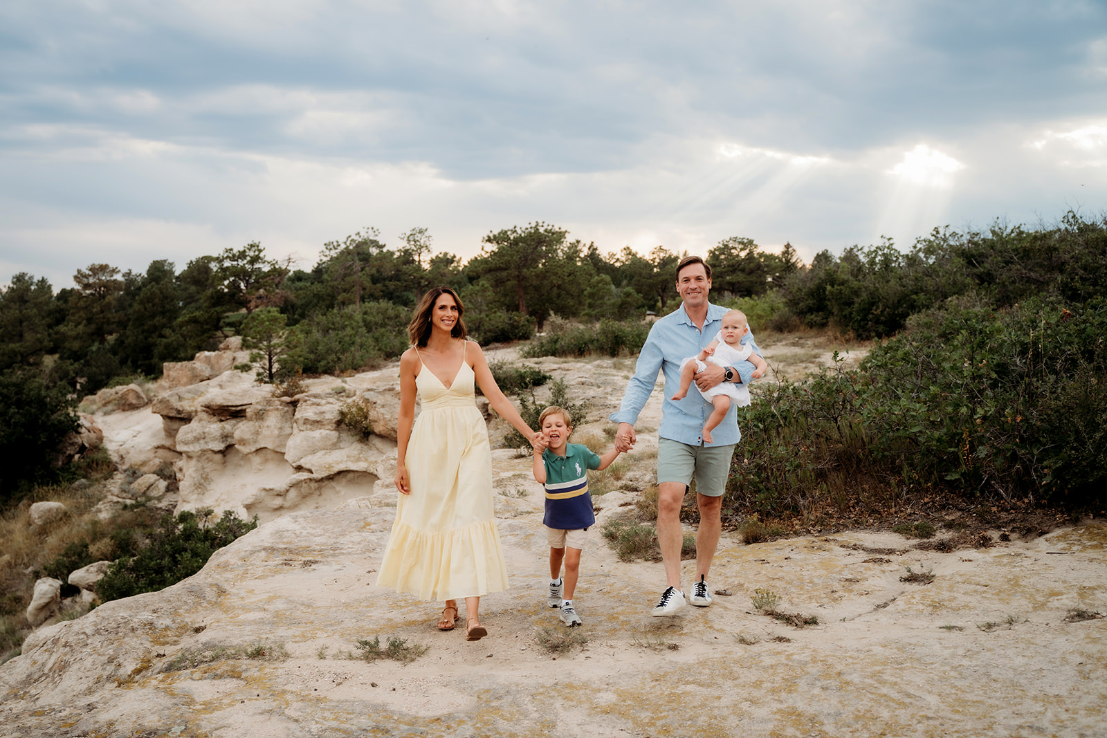 Parents walking with their children across a rocky cliffside, holding hands and smiling—natural movement is one of the most valuable family photo tips.