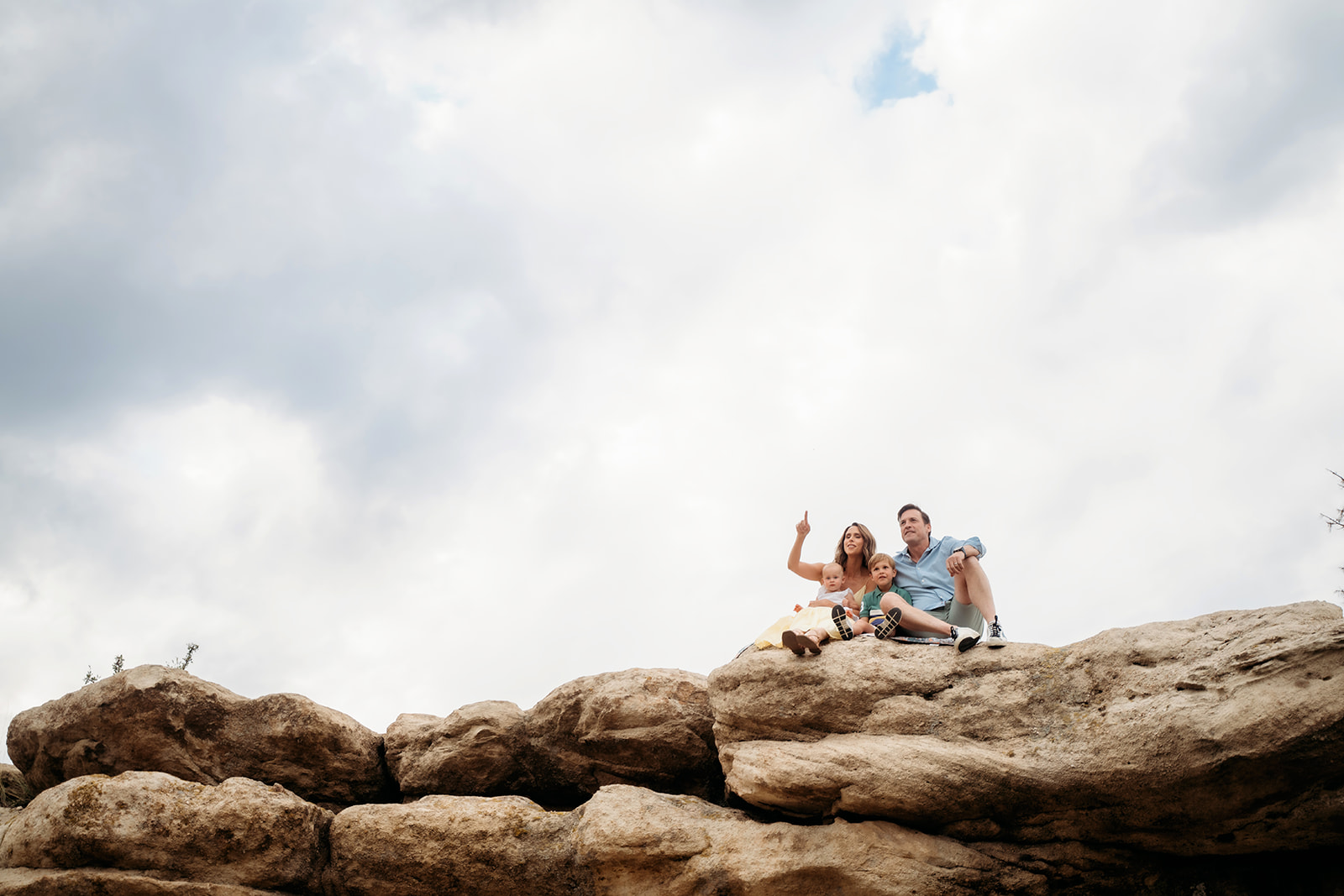 Family relaxing together on top of a massive rock formation, waving playfully toward the camera.