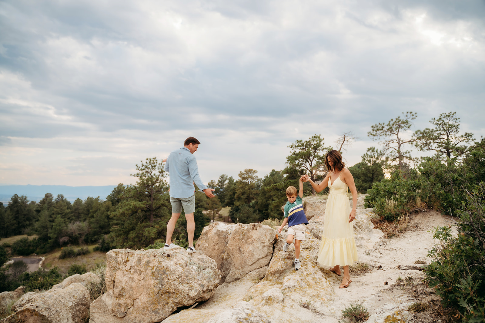 Parents helping their son climb over large rocks during a mountain photo session, working together to keep it playful and stress-free.