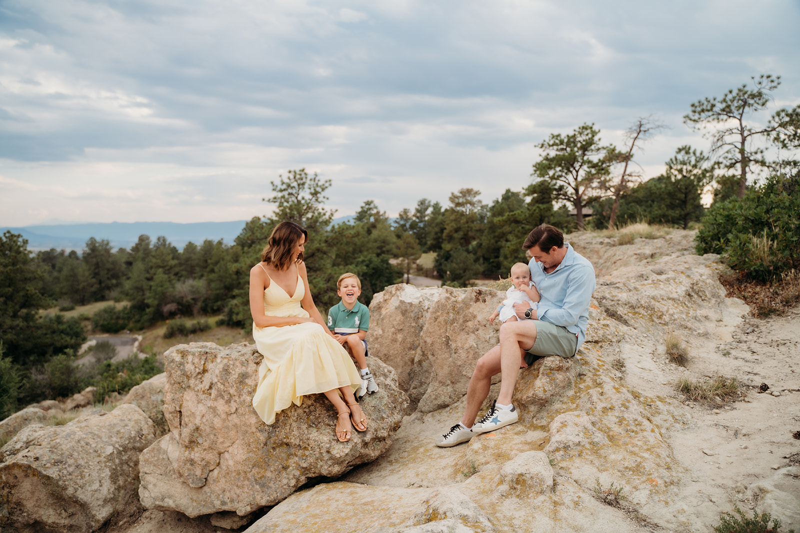 Family of four enjoying a quiet moment seated on large rocks in a scenic Colorado landscape.