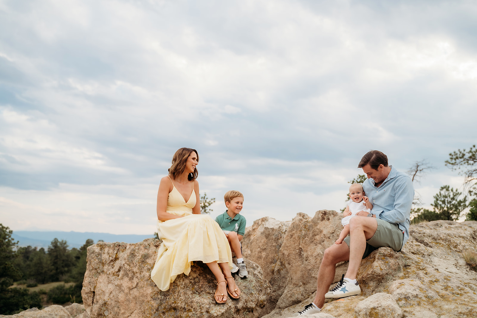 A family of four enjoying a lighthearted moment on rocky terrain under a dramatic Colorado sky.