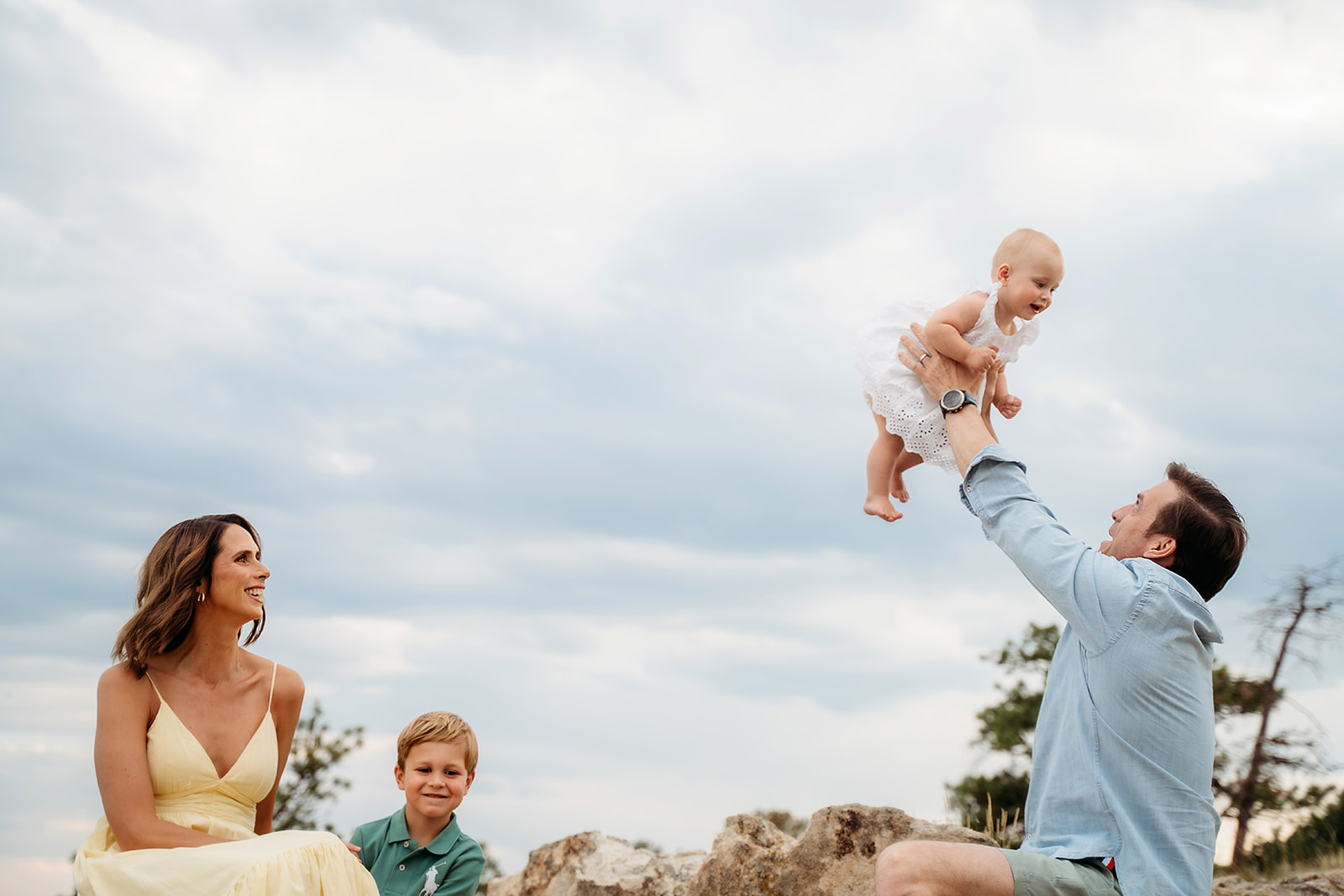 Dad lifting baby daughter into the air while mom and brother smile, enjoying the candid joy of the moment.