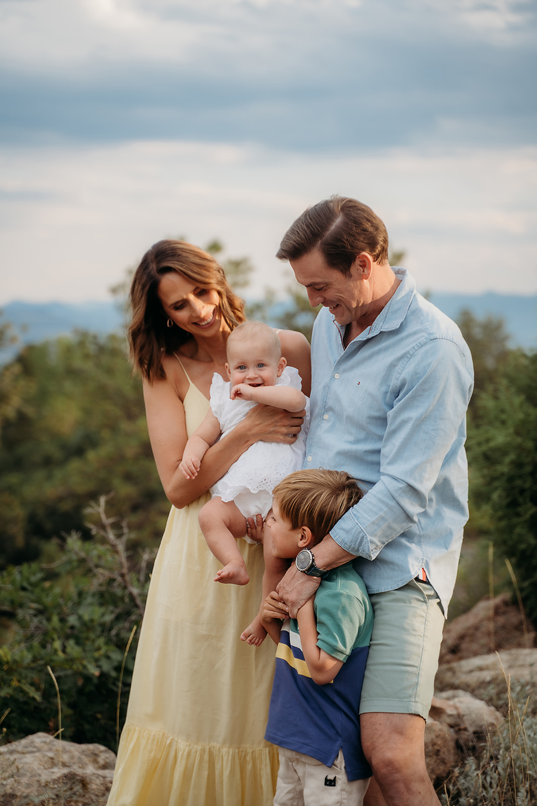 Parents cuddling their kids during a mountain session, with soft light and smiles that reflect authentic family connection.