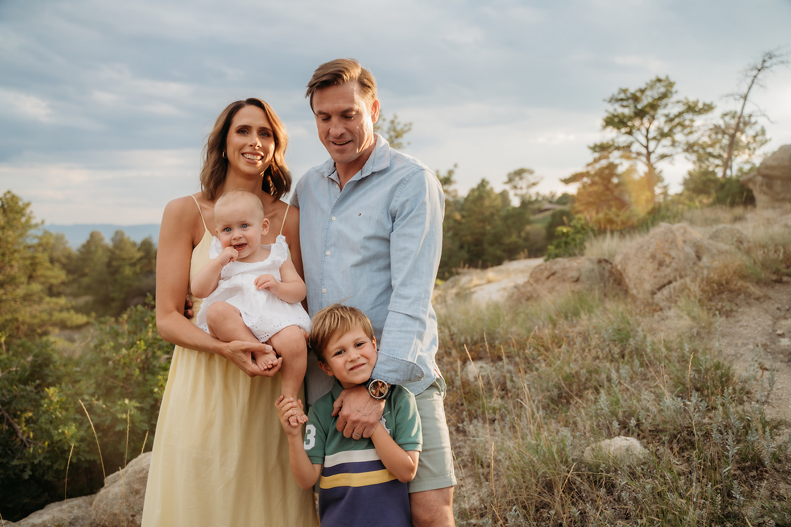 Warm sunset portrait of a family standing together in the Colorado foothills—showing how golden hour lighting enhances family photo tips.