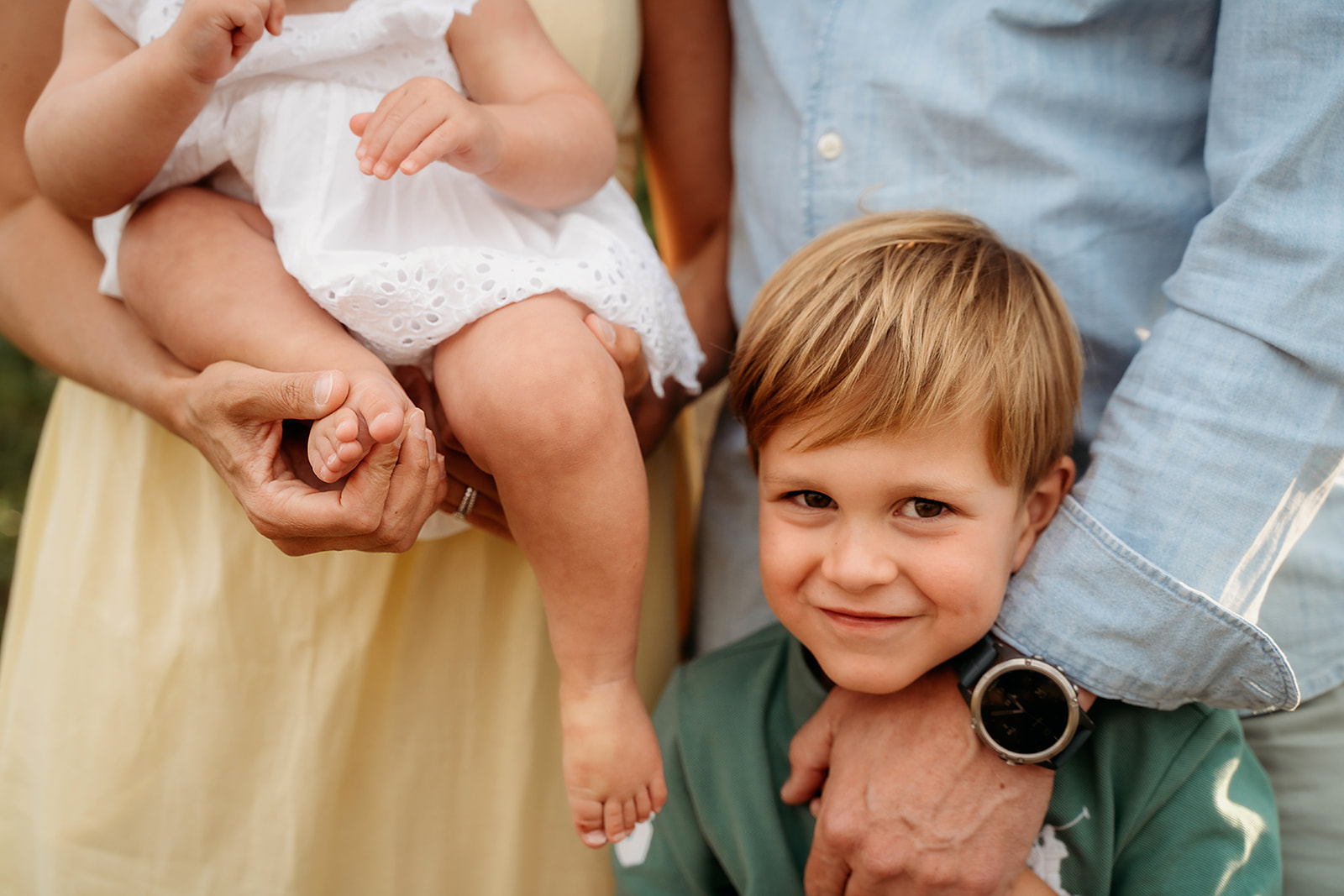 Close-up of a young boy smiling while his sister is held by their parents, illustrating the power of connection in family photo tips.