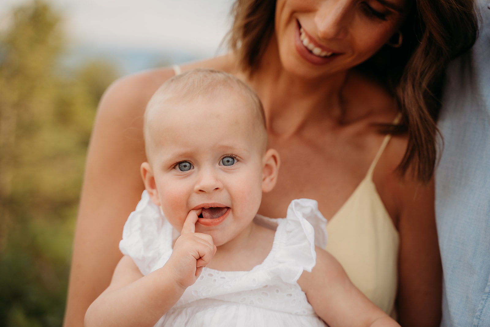 Close-up of a smiling baby girl touching her mouth while being held by her mother—candid expressions like this are gold in family photo tips.
