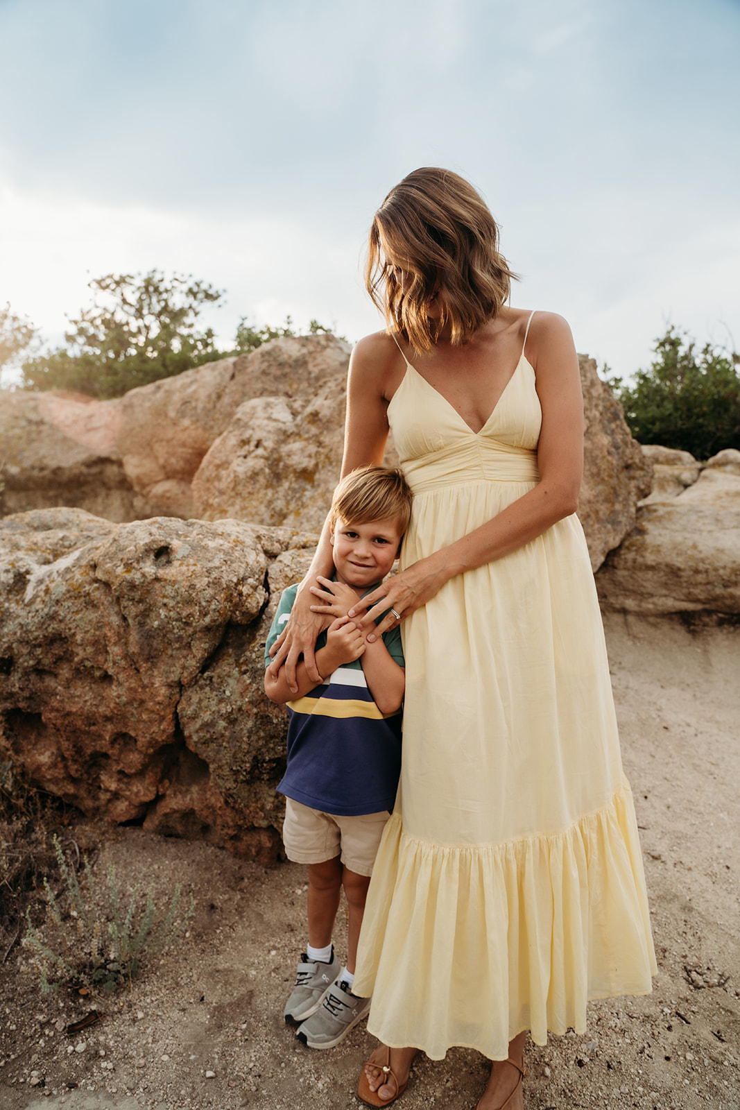 A mom hugging her young son close against her leg, capturing a quiet, tender moment that’s a favorite in family photo tips.