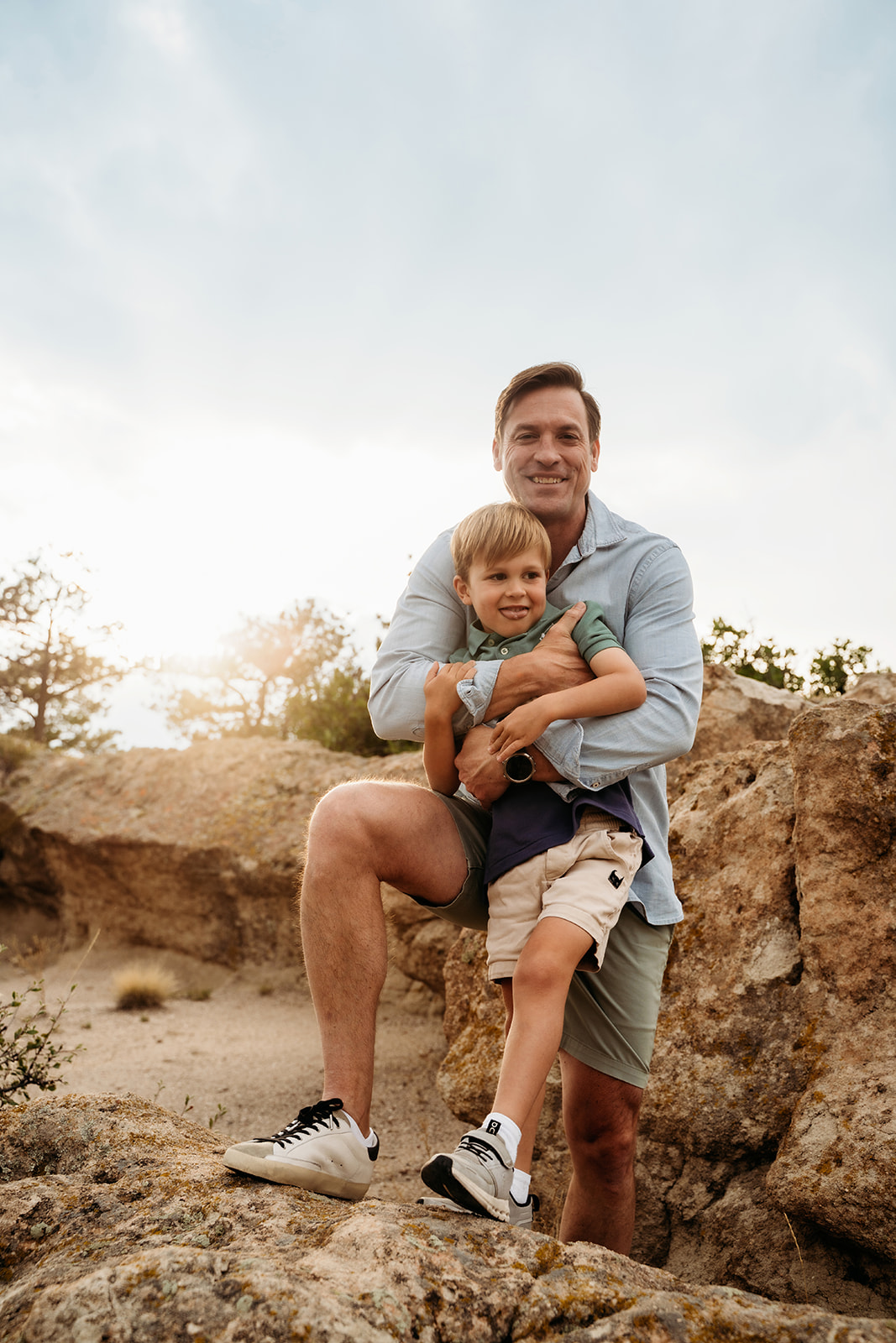 Father crouching on a rock while holding his young son, both beaming—real connection is one of the best family photo tips.