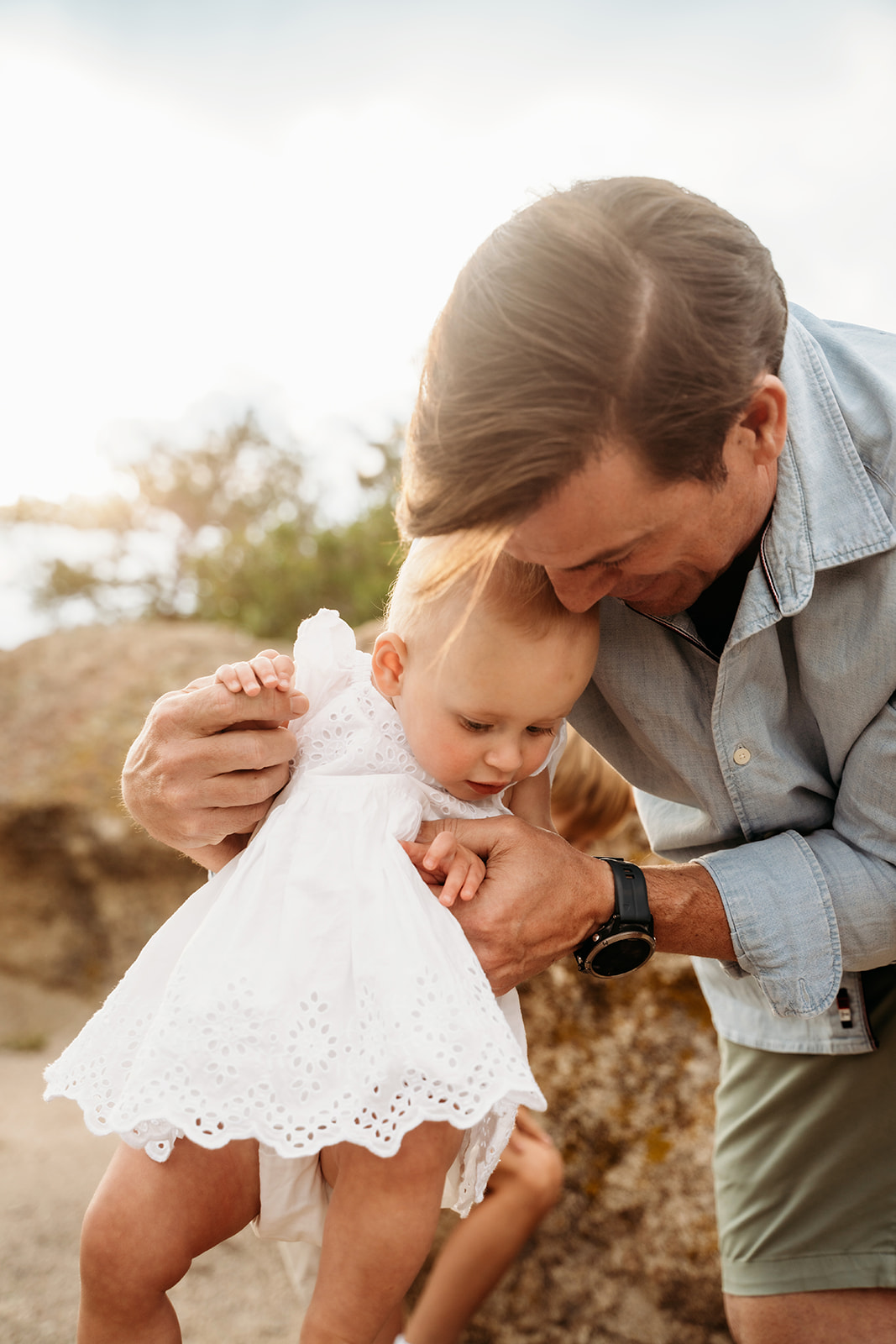 Dad leaning down to guide his toddler daughter across a rocky trail, full of love and support.