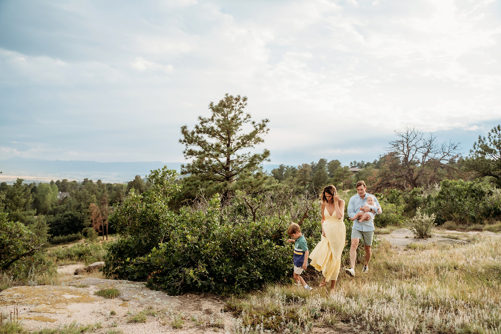 A young family walking through a Colorado meadow, surrounded by lush greenery and soft afternoon light.
