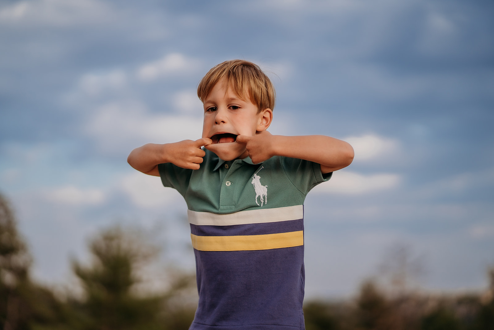 Young boy making a silly face outdoors, showcasing a fun candid moment—one of many family photo tips is to let kids be themselves.