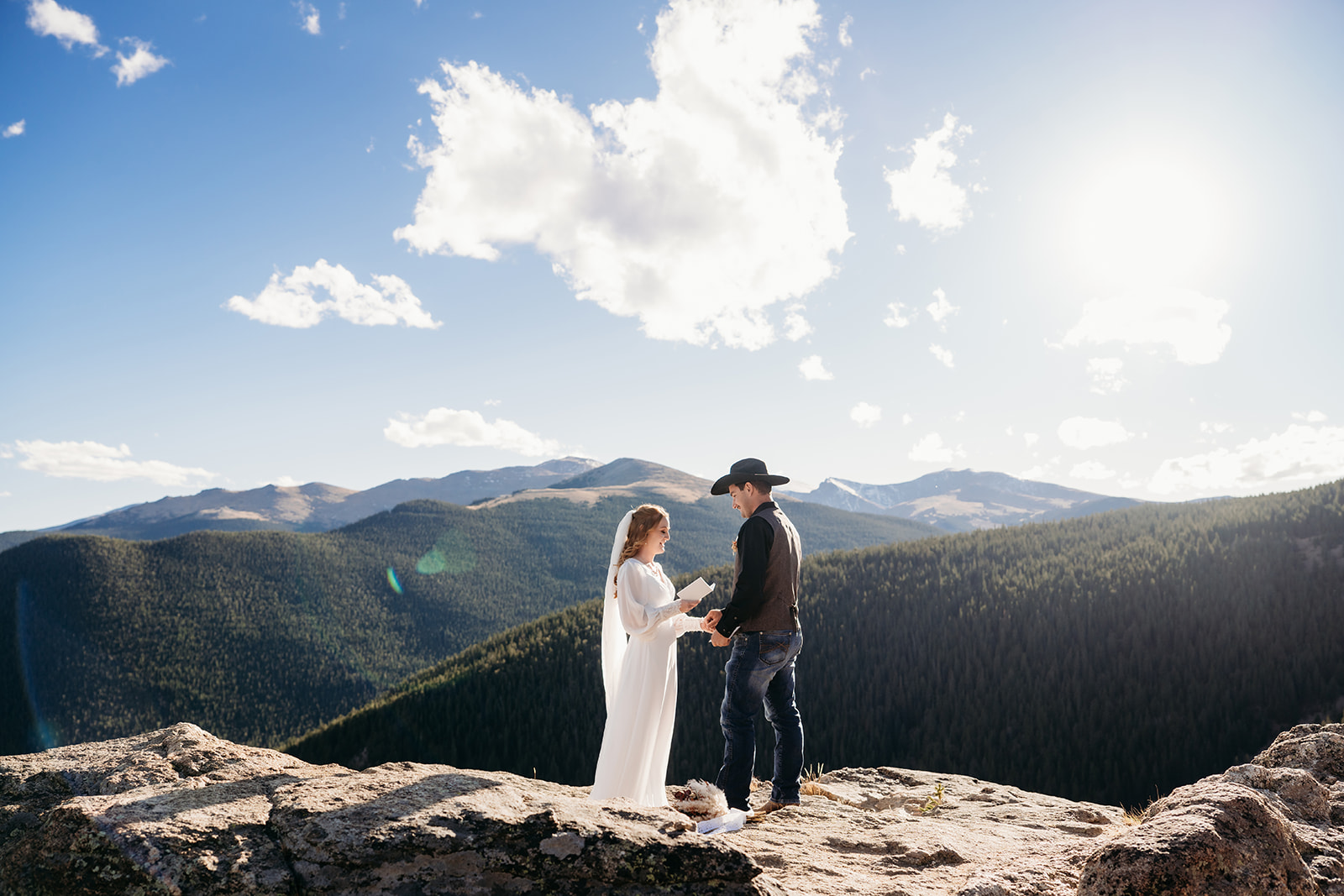 Bride holding vow book and smiling at groom under a bright Colorado sky—perfect visual for couples wondering how to write vows for an adventurous elopement.