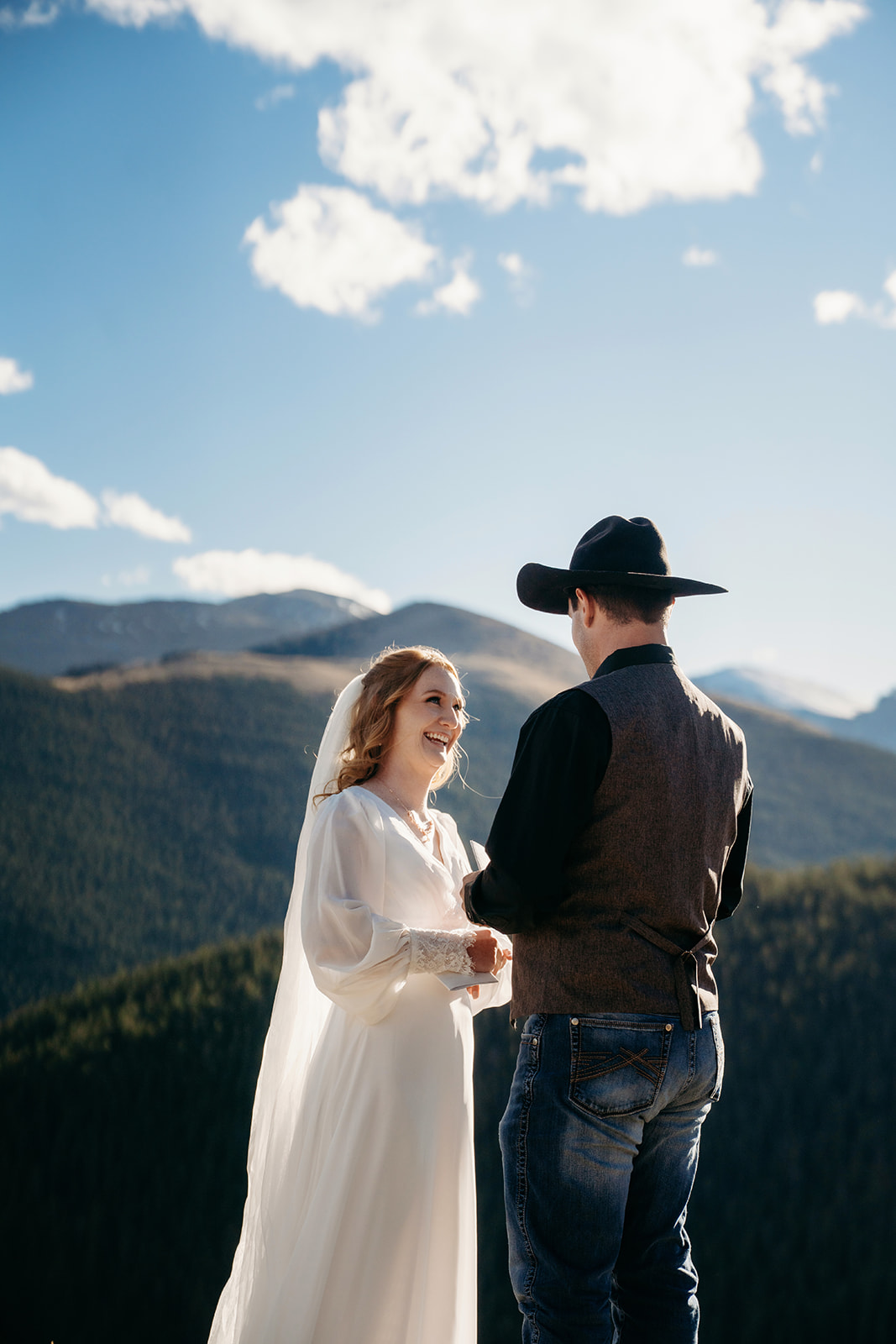 Couple exchanging vows on a sunny Colorado mountaintop, sharing laughter and heartfelt words as they learn how to write vows that reflect their story.
