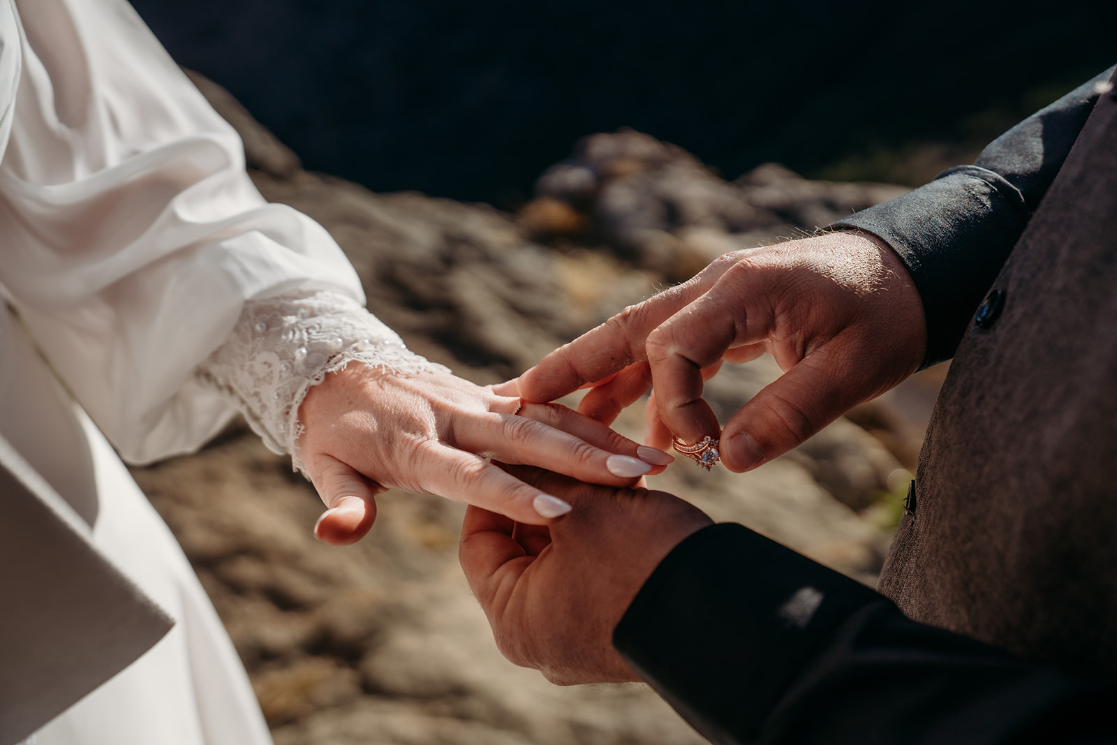 Close-up of groom placing wedding ring on bride’s finger during their mountain elopement ceremony.