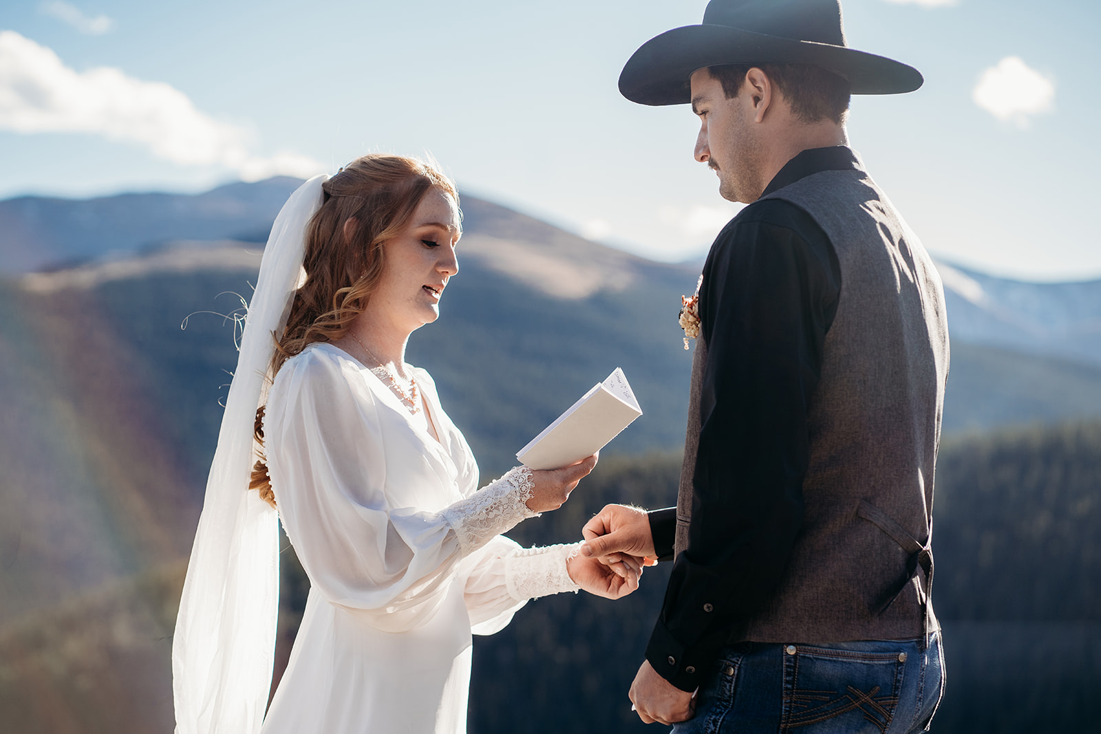 Bride reads her handwritten vows to groom, framed by mountain peaks and sunlight—an inspiring moment for how to write vows that are personal and meaningful.