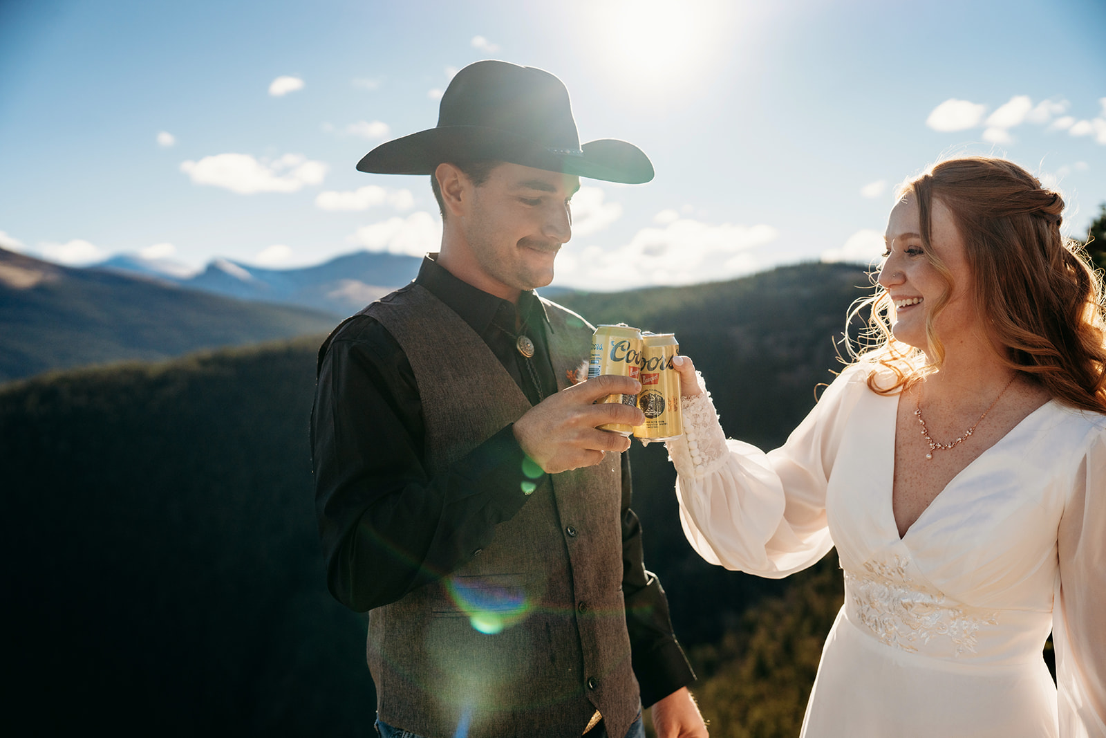 Bride and groom clink cans of Coors Banquet mid-celebration under the Colorado sun, showing their playful side after figuring out how to write vows that felt true to them.
