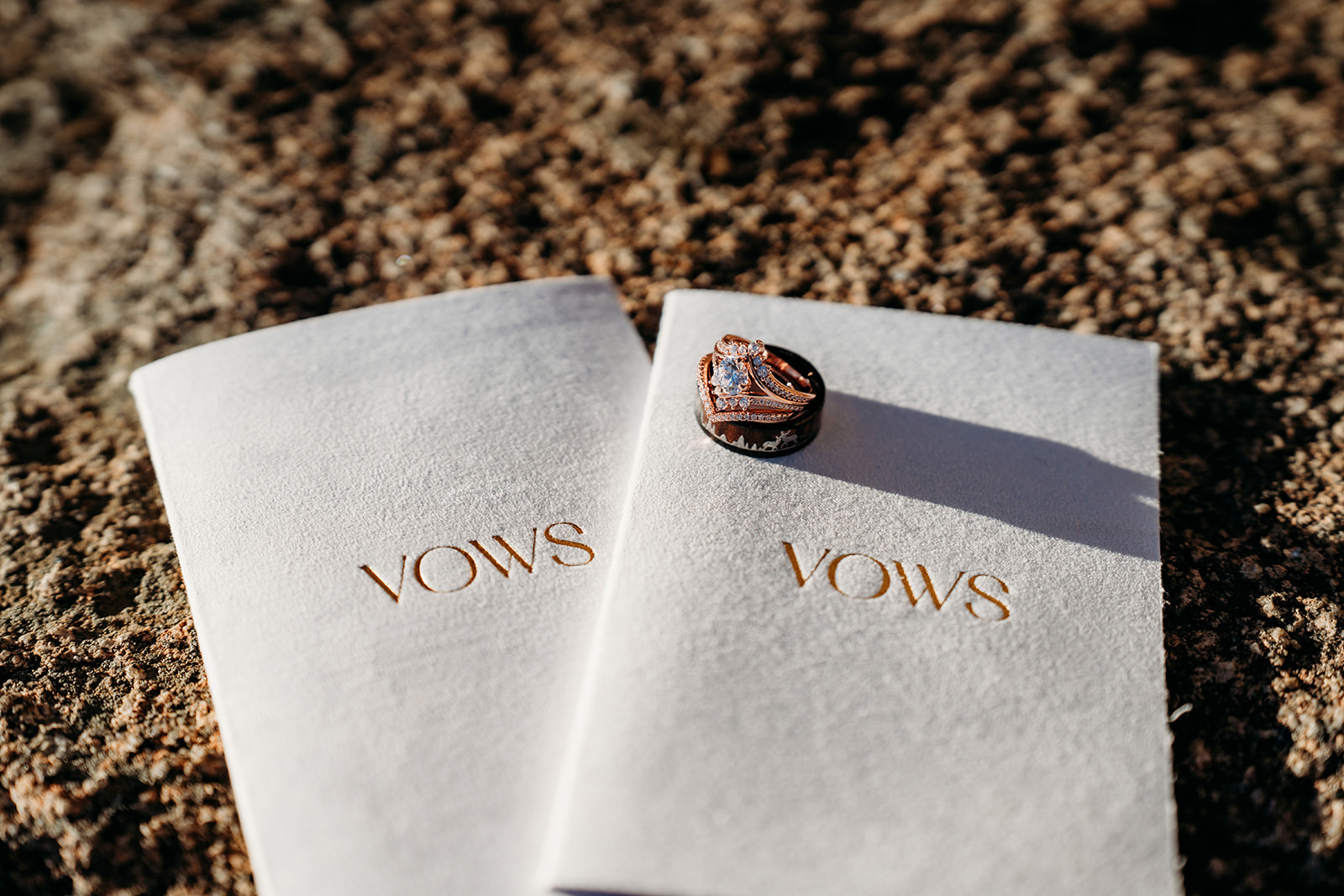 Close-up of wedding rings resting on matching vow booklets atop rugged Colorado rock—how to write vows captured in one beautiful flat lay.