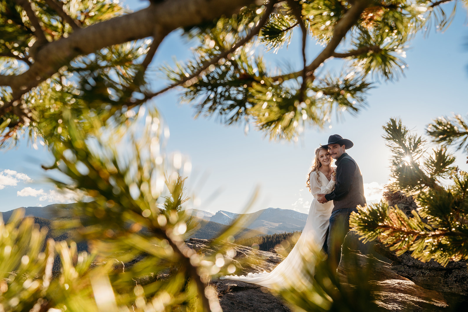 Couple framed by pine branches and golden light, holding each other after saying “I do.”