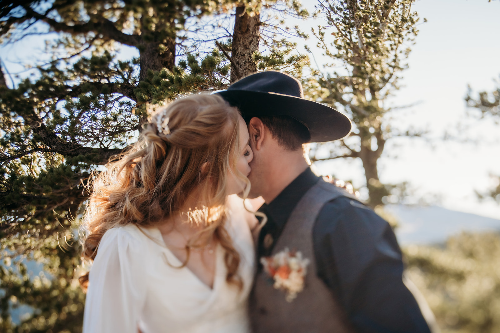 Close-up of bride whispering into groom’s ear as golden light filters through pine trees—one of many quiet moments that remind couples why knowing how to write vows from the heart matters.