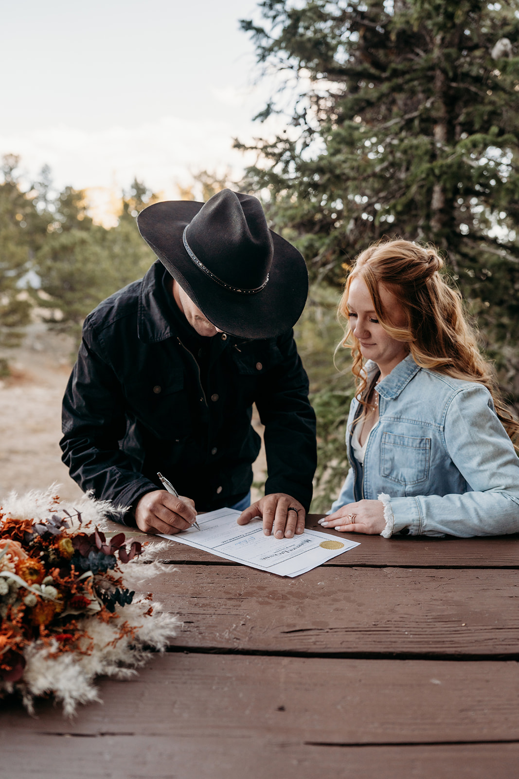Groom signs the wedding license while bride looks on, completing the paperwork after a meaningful ceremony and the exchange of handwritten vows.