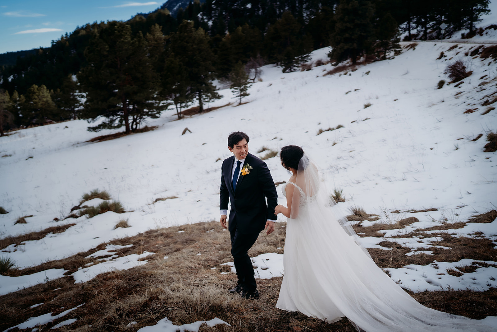 Bride and groom share a glance while walking uphill through a snowy Colorado field.