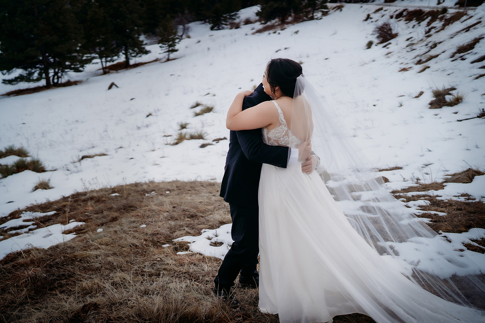 Bride and groom embrace on a snowy hillside during their Colorado winter wedding.
