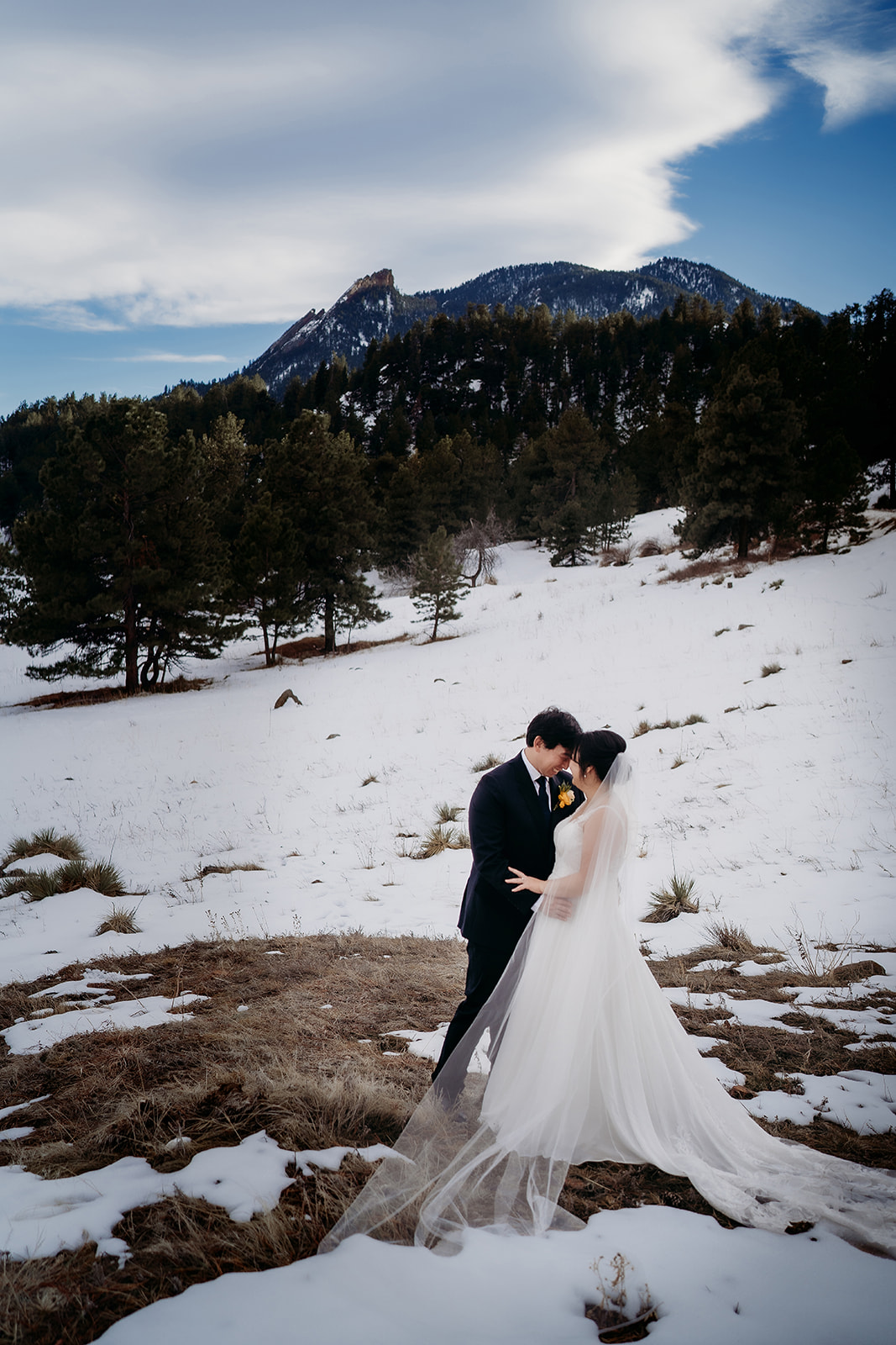 Couple kisses in a snowy Colorado meadow, mountains in the background during their winter wedding.