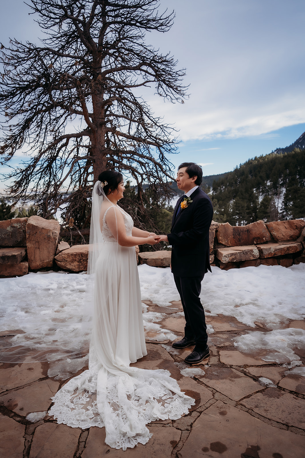 Couple holding hands during an emotional ceremony surrounded by snow and pines.