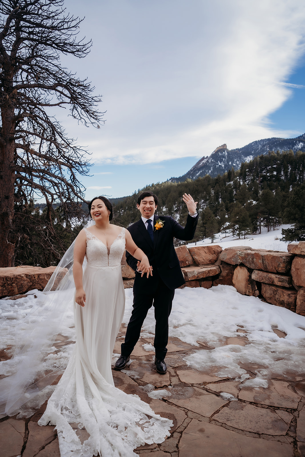 Bride and groom laughing and waving in a snowy mountain ceremony space with scenic views.