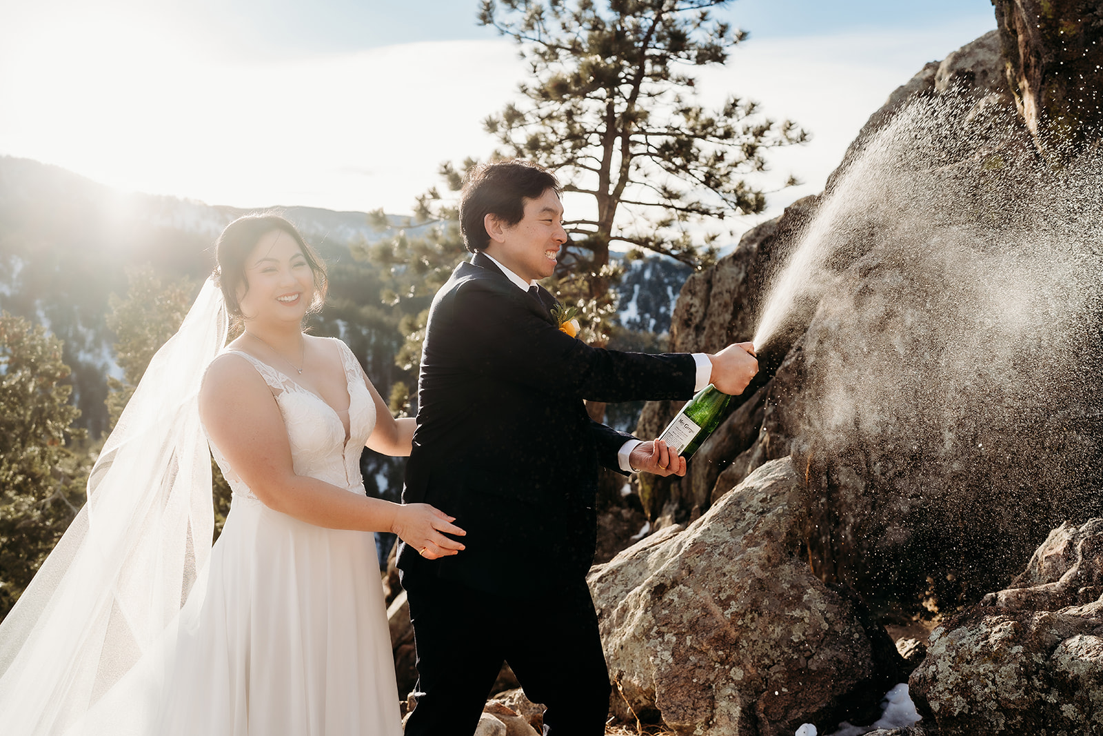Bride laughs while groom sprays champagne in celebration during their Colorado winter wedding.