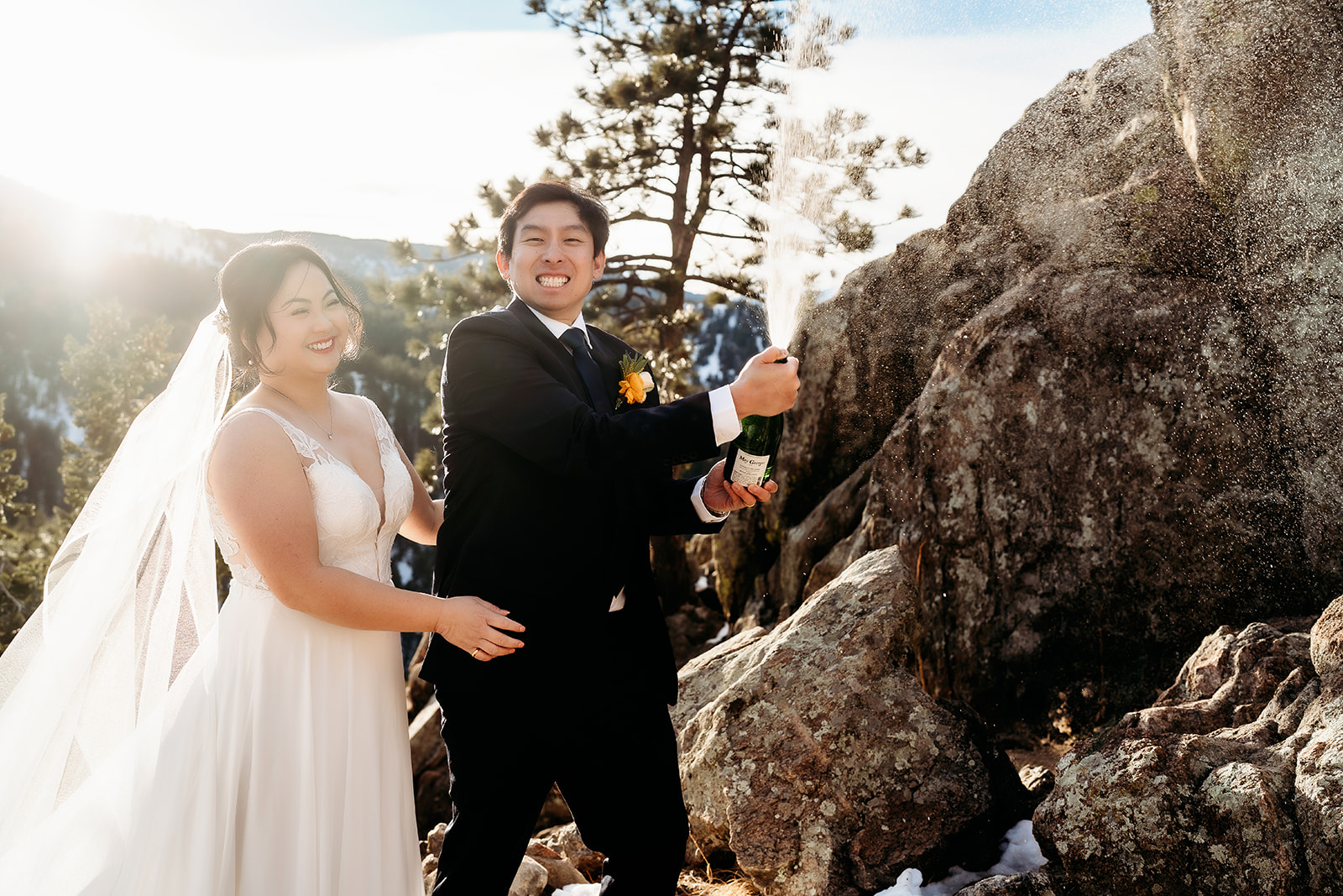 Groom pops a champagne bottle while the bride smiles during their Colorado winter wedding celebration.