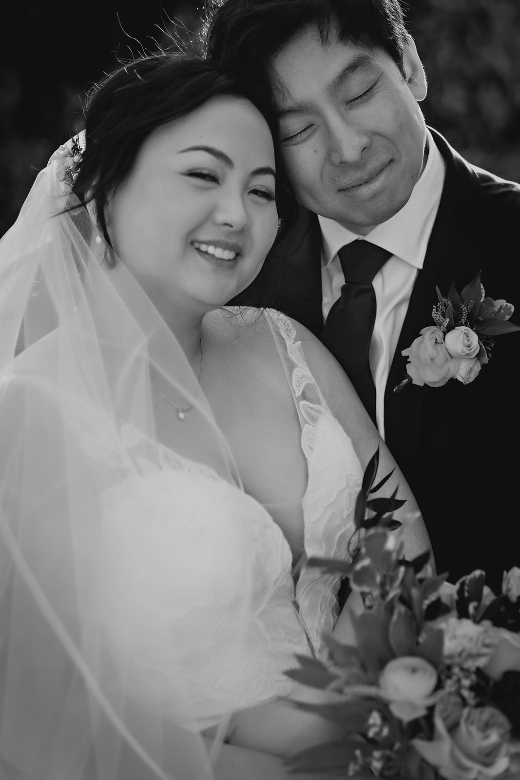 Close-up black-and-white portrait of the newlyweds cuddling and smiling with soft floral details.