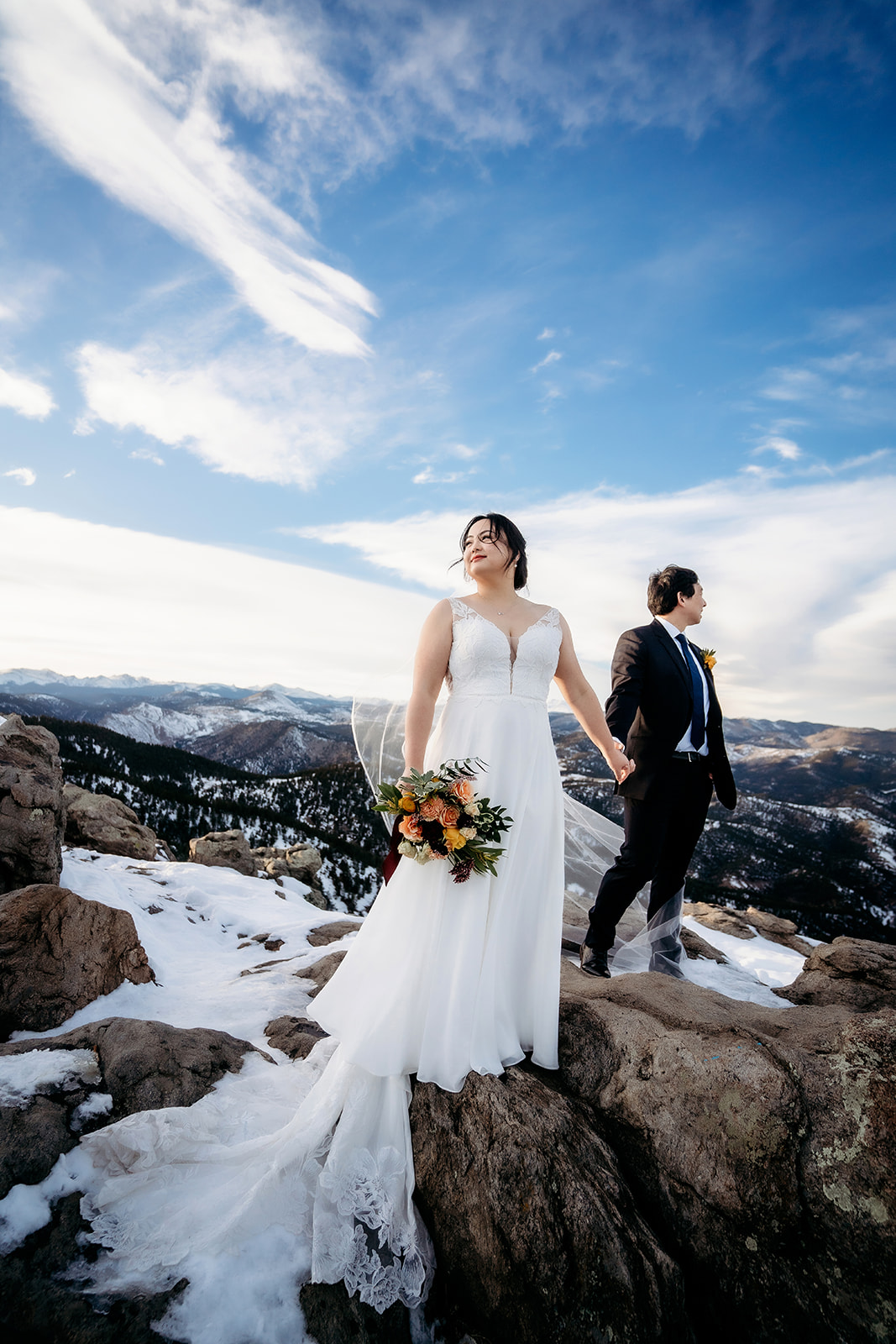 Bride and groom hold hands on a rocky overlook during their adventurous Colorado winter wedding.