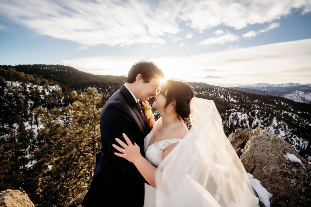 Bride and groom share a joyful forehead-to-forehead moment at their Colorado winter wedding with mountains behind them.