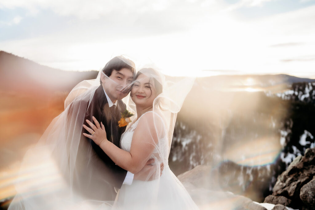Dreamy photo of couple wrapped in a veil, glowing with joy against snowy Colorado peaks.