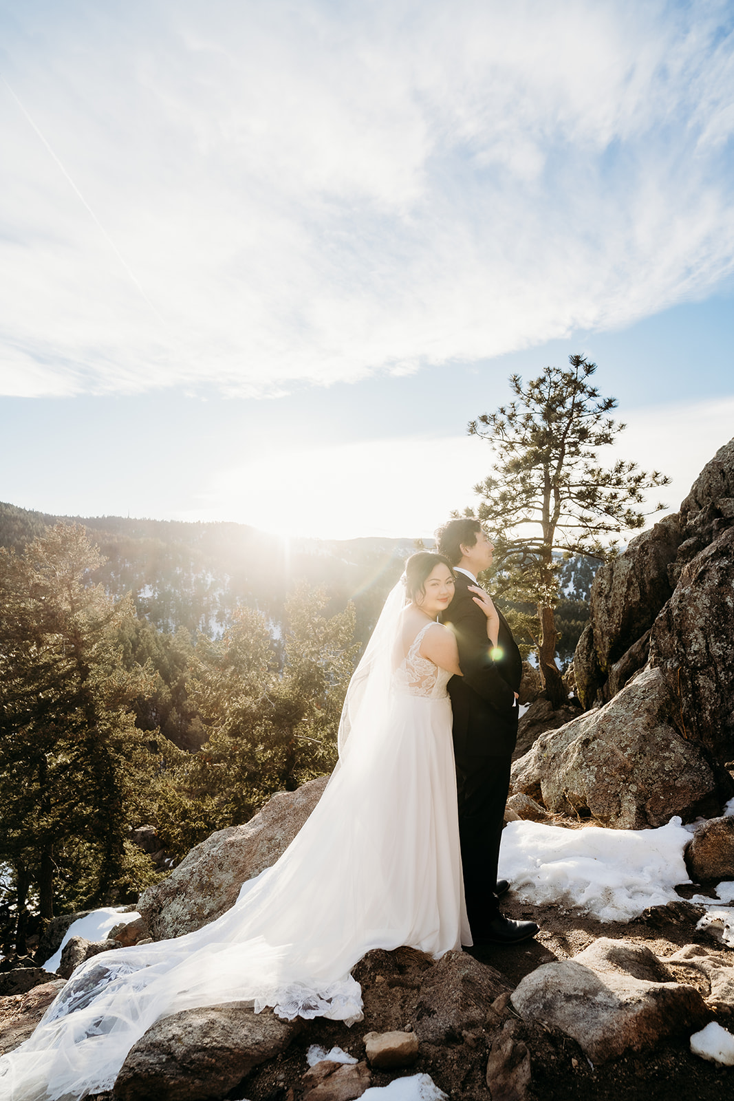 Bride and groom pose on a snow-dusted rock ledge at their Colorado winter wedding.